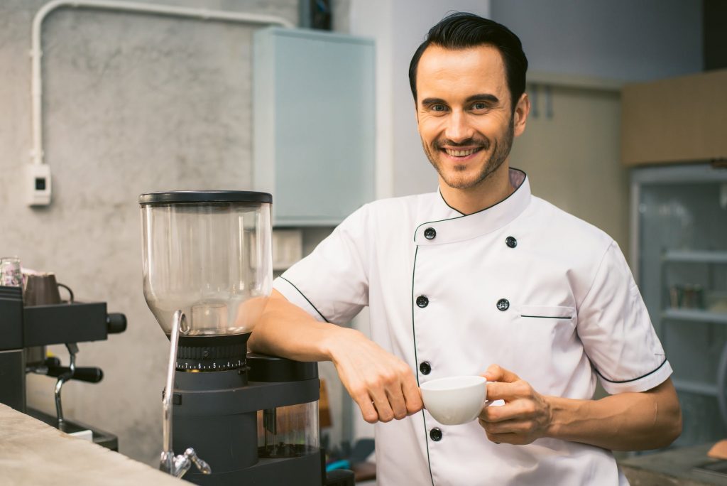 barista next to coffee machine holding coffee cup