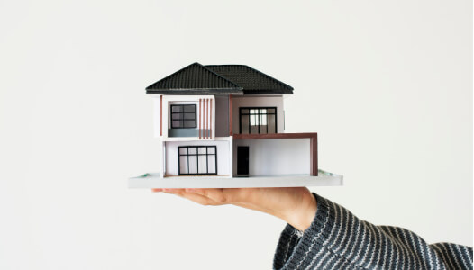 person lifting up a model house atop their palm